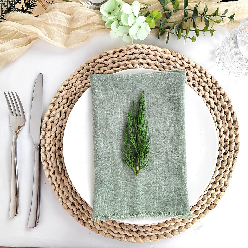 Élégante table de salle à manger avec sets de table en fibres naturelles, assiettes et couverts, serviette verte décorative avec branche de cèdre.