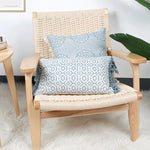 Un fauteuil en rotin naturel avec des coussins bleus ornés de motifs géométriques, installé dans un intérieur lumineux et apaisant.