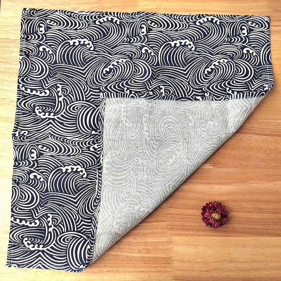 Une couverture noire et blanche motif vagues décorée d'une fleur violette sur un sol en bois.