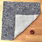 Une couverture noire et blanche motif vagues décorée d'une fleur violette sur un sol en bois.