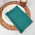 Un service de table en rotin tressé supportant une assiette blanche et un linge de table vert.