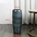 Un grand vase gris décoratif de 52 cm de hauteur et 15 cm de diamètre, posé sur un sol en bois.