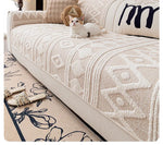 Un chat blanc repose sur un canapé avec un motif géométrique texturé, aux côtés de coussins décoratifs et d'un tapis orné de motifs floraux.