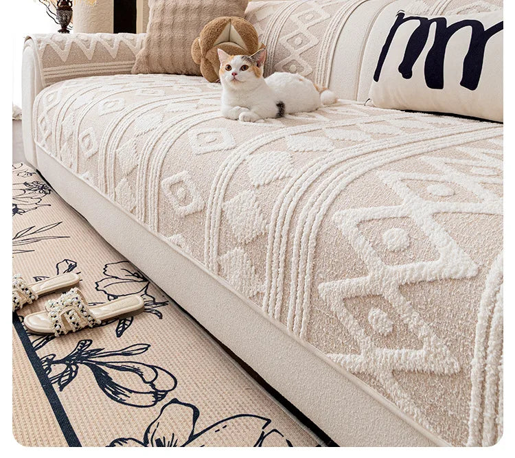 Un chat blanc repose sur un canapé avec un motif géométrique texturé, aux côtés de coussins décoratifs et d'un tapis orné de motifs floraux.