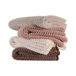 Pile de couvertures douces et moelleuses dans des tons de beige, rose et marron, offrant une texture agréable et une apparence accueillante.