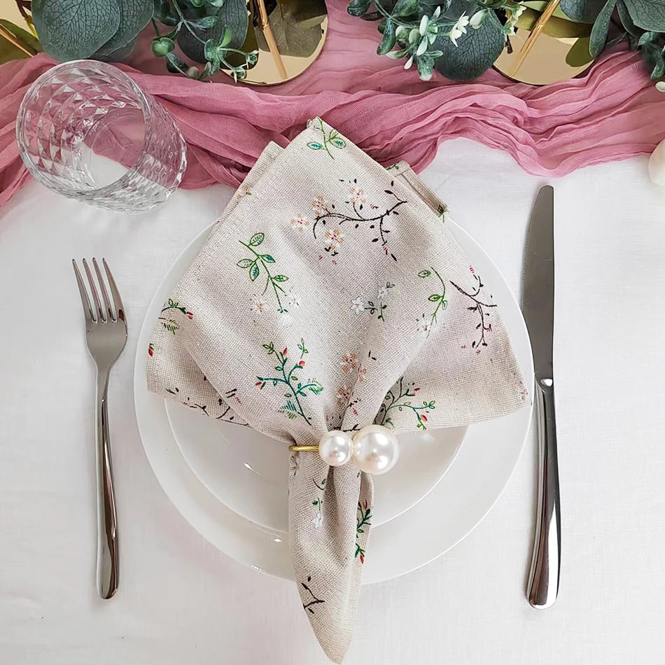 Une belle nappe blanche brodée de fleurs vertes, décoré de perles, posée sur une table avec des couverts argentés et un verre de cristal.