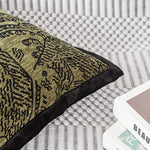 Coussin décoratif avec motif abstrait en couleurs or et noir, posé sur un canapé à texture gris clair.