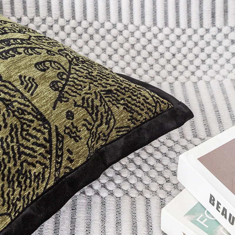 Coussin décoratif avec motif abstrait en couleurs or et noir, posé sur un canapé à texture gris clair.