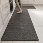Un tapis gris motif tissé au sol d'une cuisine, avec des pieds nus posés dessus.