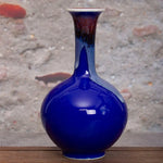 Vase en céramique bleu de forme sphérique avec un col allongé et de belles nuances rougeâtres sur la surface.