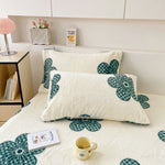 Coussins moelleux ornés de fleurs stylisées de couleur vert émeraude sur fond blanc, créant une ambiance chaleureuse et confortable dans la pièce.