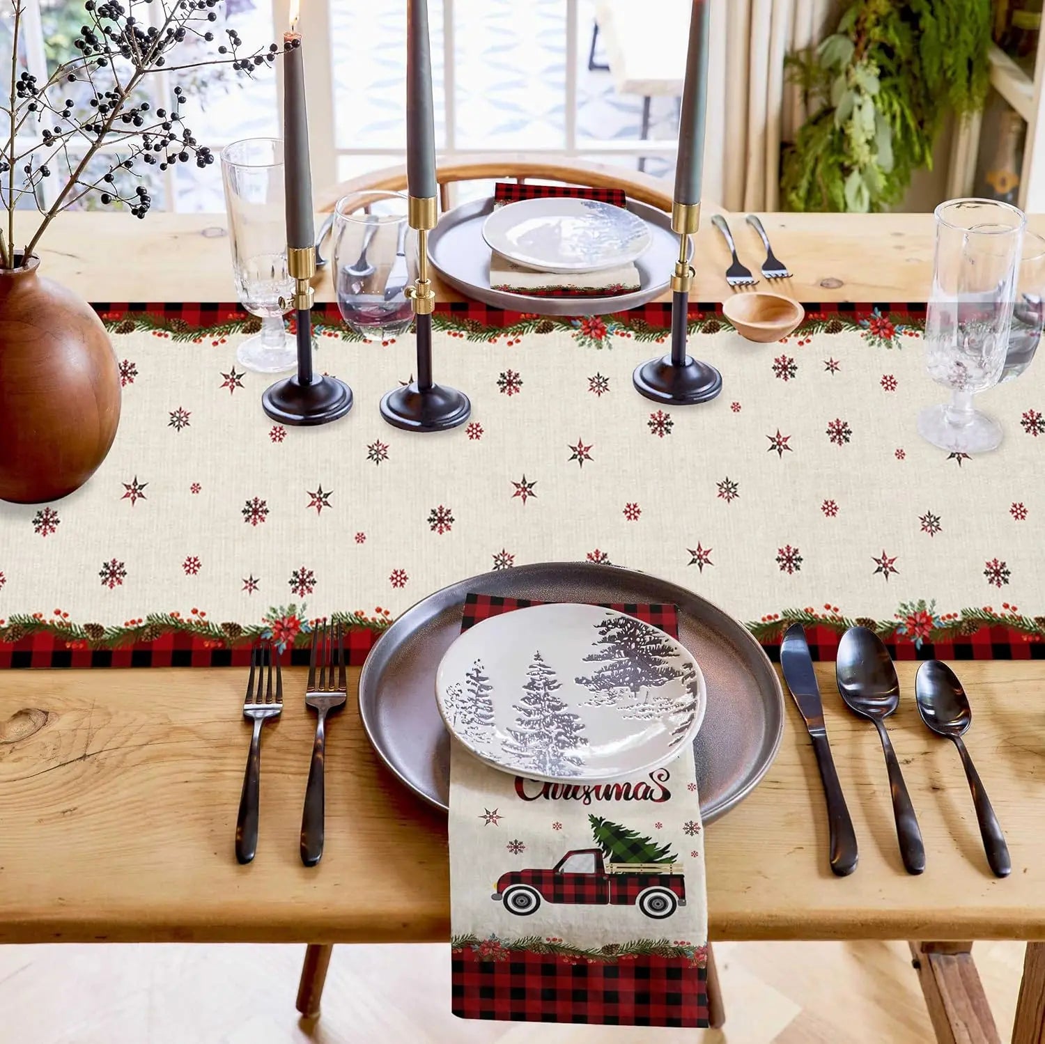 Magnifique table de Noël avec des bougies, des assiettes et des couverts sur un tissu décoré de motifs de flocons de neige et d'un camion transportant un arbre de Noël.