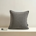 Coussin décoratif gris avec des rayures texturées, posé sur une surface blanche avec un porte-stylo en verre.