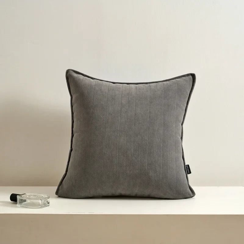Coussin décoratif gris avec des rayures texturées, posé sur une surface blanche avec un porte-stylo en verre.