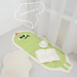 Une peluche verte avec des yeux et une bulle de pensée indiquant "confortable" tient un livre ouvert, créant une scène confortable et accueillante.