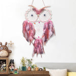 Un rêve d'attrape-rêves rose et blanc, décoré de plumes et de détails floraux, suspendu au mur au-dessus d'une étagère ornée de figurines et de plantes.