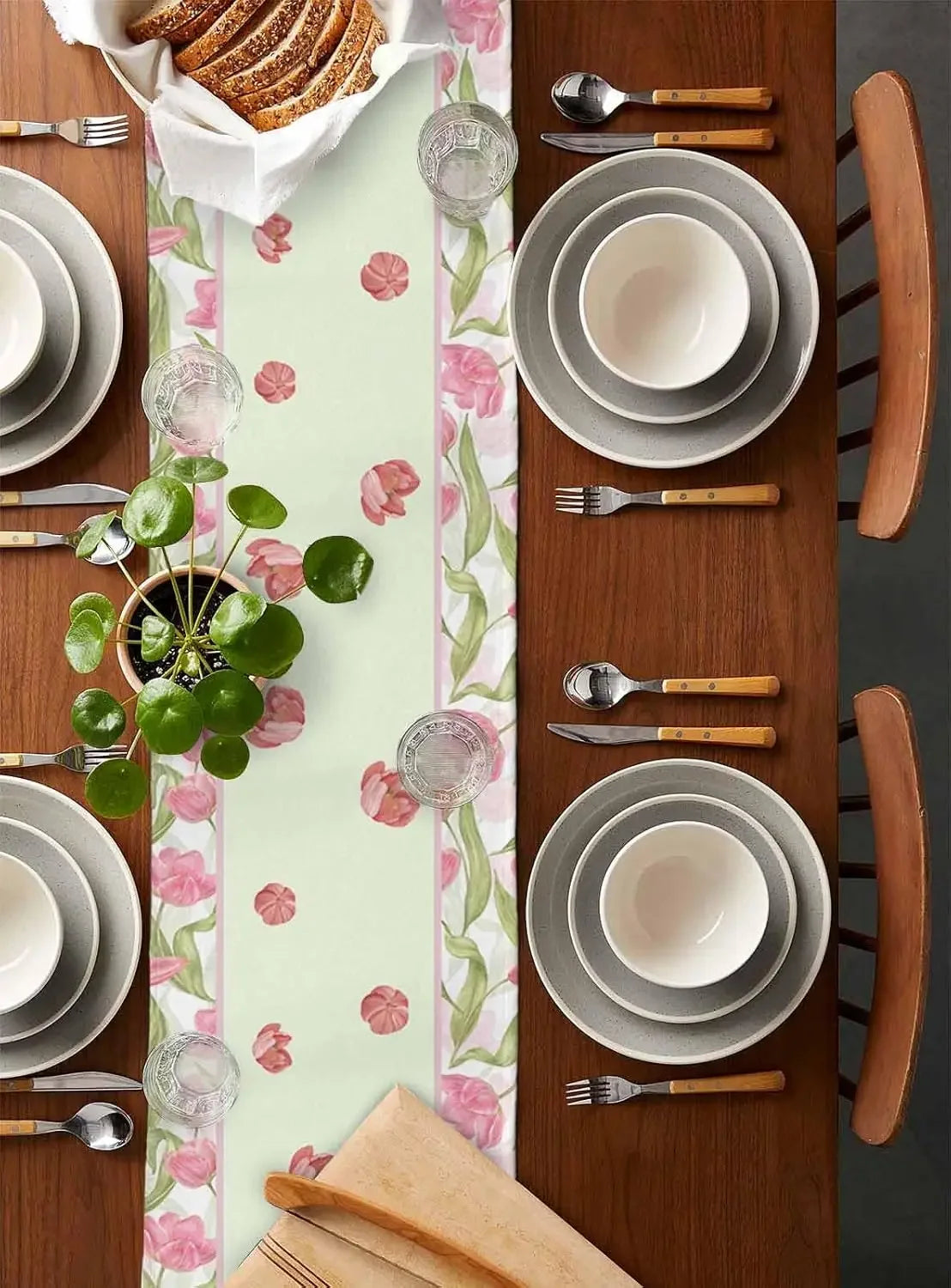 Une table dressée avec un motif fleuri, des assiettes et des couverts en bois, accompagnée d'un panier de pain et d'un plat de verdure.