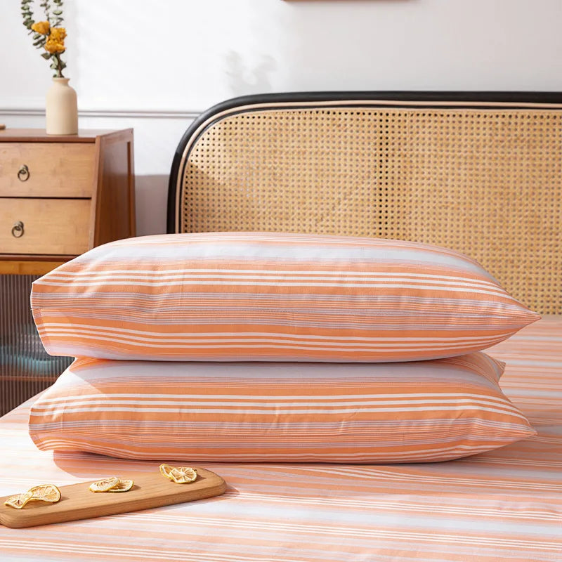 Deux oreillers recouverts d'une housse rayée orange et blanche, reposant sur un lit ancien avec un cadre en cannage.