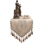 Sur cette image, on peut voir une élégante statuette en bronze représentant une figure féminine drapée, posée sur un magnifique coussin décoratif beige brodé de motifs floraux avec des pompons.