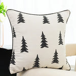 Coussin décoratif avec des motifs d'arbres noirs stylisés sur un fond blanc.