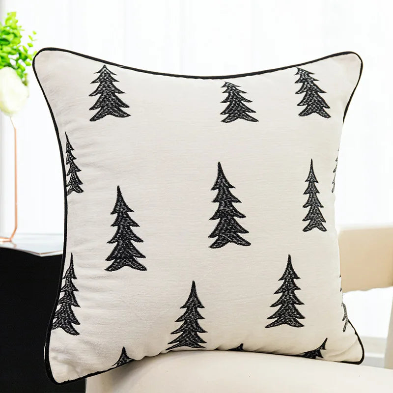 Coussin décoratif avec des motifs d'arbres noirs stylisés sur un fond blanc.