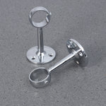 Deux supports chromés solides pour tringle à rideaux, disposés sur un sol gris texturé.