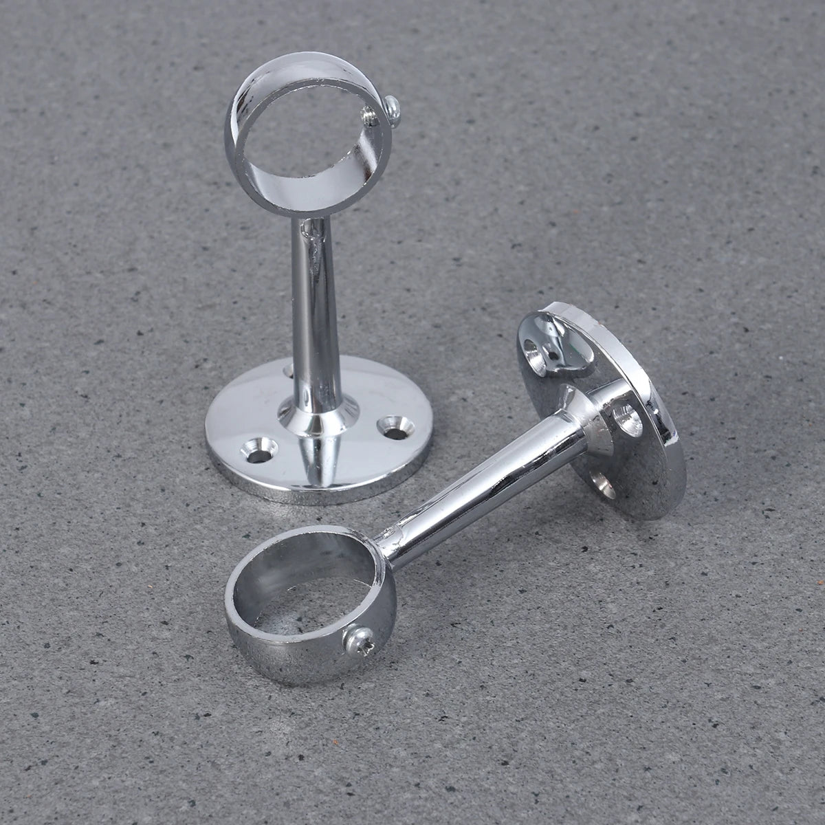 Deux supports chromés solides pour tringle à rideaux, disposés sur un sol gris texturé.