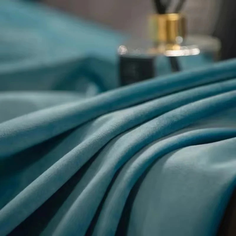 Zoom sur les plis d’un rideau en velours bleu clair illuminé, avec un flacon de parfum en arrière-plan flouté.