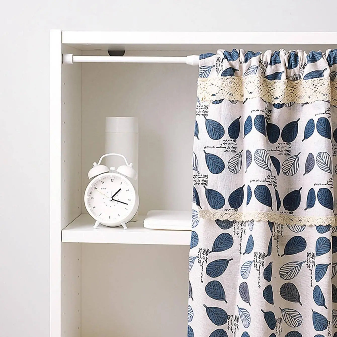 Tringle à rideaux sans perçage placée dans une étagère blanche pour suspendre un rideau décoratif.