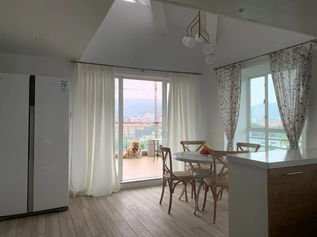 Vue intérieure d’une salle à manger avec tringles à rideaux vintage et rideaux blancs sur baie vitrée