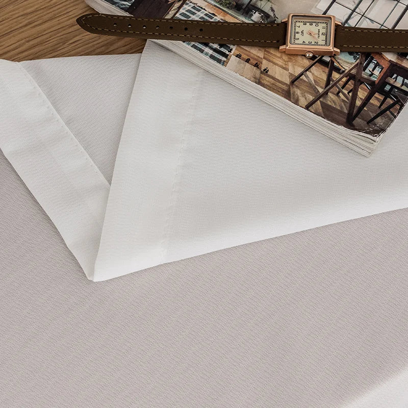 Zoom sur les finitions couture d’un voilage blanc, avec une montre et un magazine en décoration.