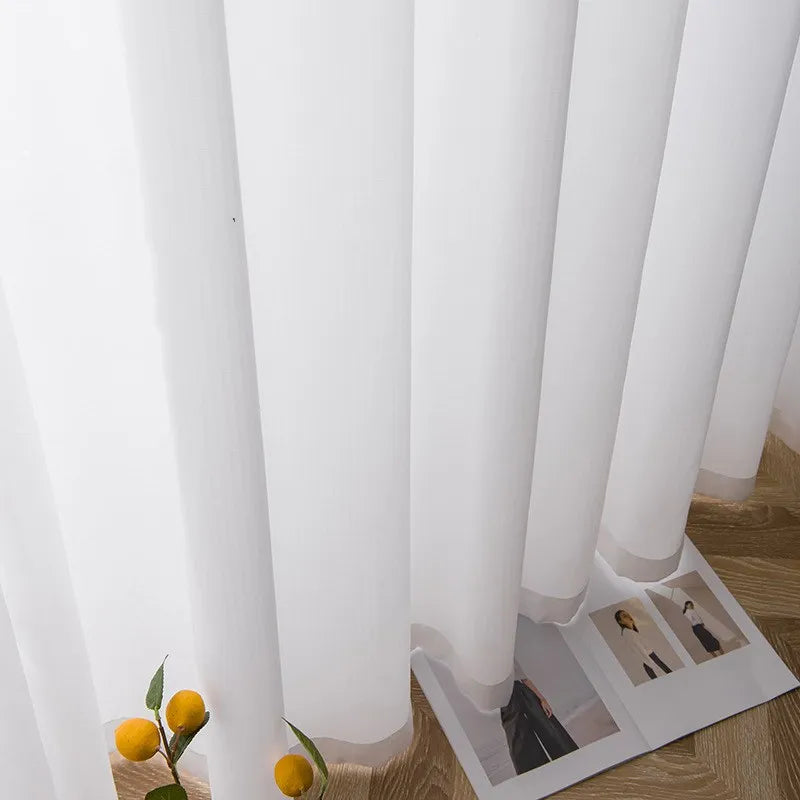 Voilage blanc à galon fronceur tombant en plis harmonieux sur le sol, accompagné de touches déco naturelles