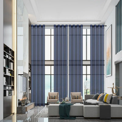 Voilage bleu marine suspendu dans un salon moderne avec plafond haut et grandes baies vitrées, créant une ambiance élégante et lumineuse.