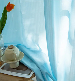 Voilage bleu en 140 x 220 installé près d’une fenêtre, avec une tulipe orange et une théière blanche sur table pour une ambiance zen.