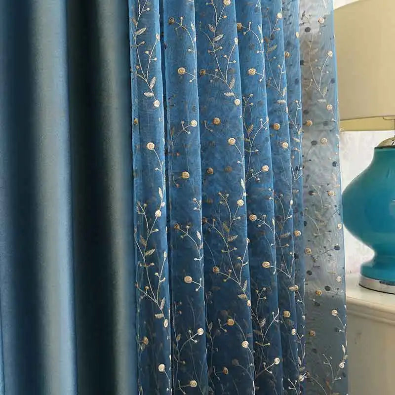 Zoom sur un voilage fin bleu avec des broderies végétales dorées, placé devant un rideau opaque bleu nuit.