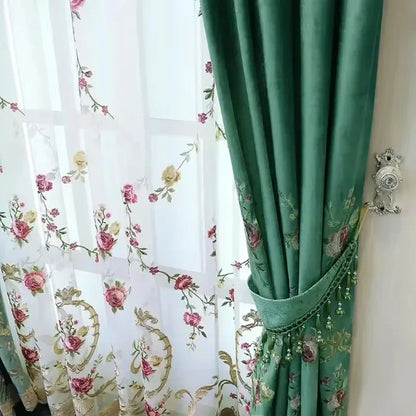 Vue rapprochée d’un rideau vert bouteille attaché sur le côté avec un voilage brodé floral en arrière-plan.