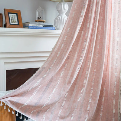 Voilage rose bohème à motifs brodés et pompons décoratifs, drapé élégamment devant une cheminée blanche dans un intérieur chaleureux et raffiné.