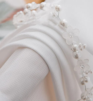 Gros plan sur le tissu du voilage blanc montrant la finesse de la maille avec une décoration florale perlée
