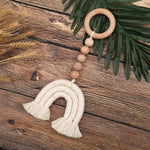 Attache décorative en forme d'arc en ciel avec perles, idéale pour la décoration murale de chambre d'enfant, posée sur une table en bois avec des feuilles vertes et des épis de blé. Accessoire tendance pour un intérieur moderne et chaleureux.