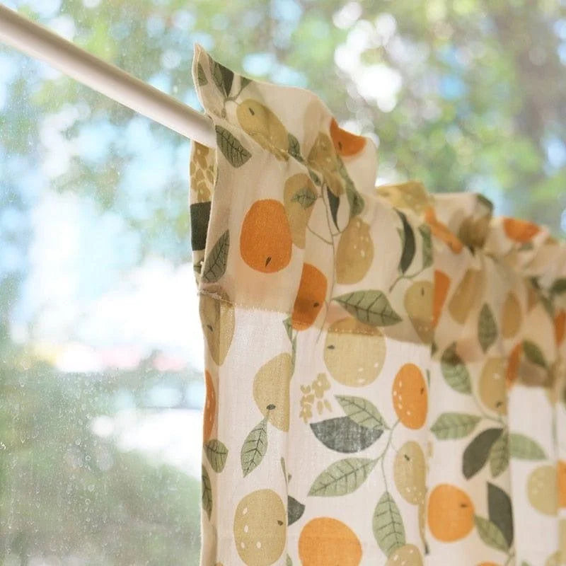 Rideau de cuisine imprimé fruits avec motif coloré de citrons et oranges, accroché à une tringle devant une fenêtre ensoleillée, créant une ambiance fraîche et lumineuse pour sublimer votre intérieur. Parfait pour ajouter une touche de gaieté et de nature à votre décoration.