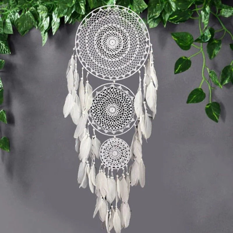 Attrape-rêves décoratif avec motifs détaillés, suspendu devant un mur gris, entouré de feuillage vert. Parfait pour la décoration intérieure bohème ou comme cadeau apaisant pour embellir vos espaces de vie. Cet attrape-rêves ajoute une touche de tranquillité et de style élégant à votre maison.
