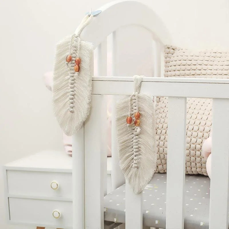 Décoration murale bohème en forme de plume blanche, ornée de perles dans les tons orangés, accrochée à un lit pour bébé. Idéale pour ajouter une touche de douceur et de style dans une chambre d'enfant.