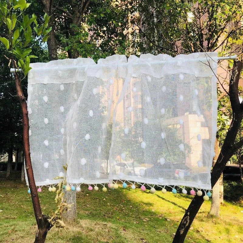 Rideau décoratif blanc avec motifs à pois et franges colorées suspendu à l'extérieur, idéal pour apporter une touche de fraîcheur et de légèreté à votre intérieur. Ce rideau tendance est parfait pour illuminer vos fenêtres tout en ajoutant une note de modernité et de joie à votre décoration. Adapté pour salon, chambre ou cuisine.