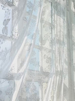 Rideaux voilages blancs imprimés papillons et fleurs installés sur une tringle argentée dans un salon cosy.