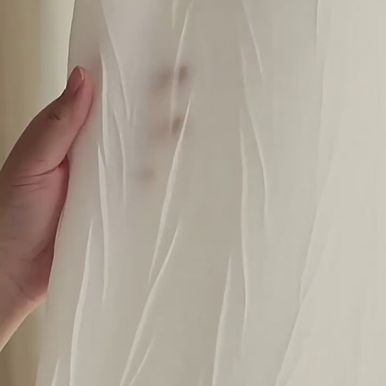 Zoom sur un voilage blanc froissé avec une main en transparence pour illustrer la légèreté et la finesse du tissu.