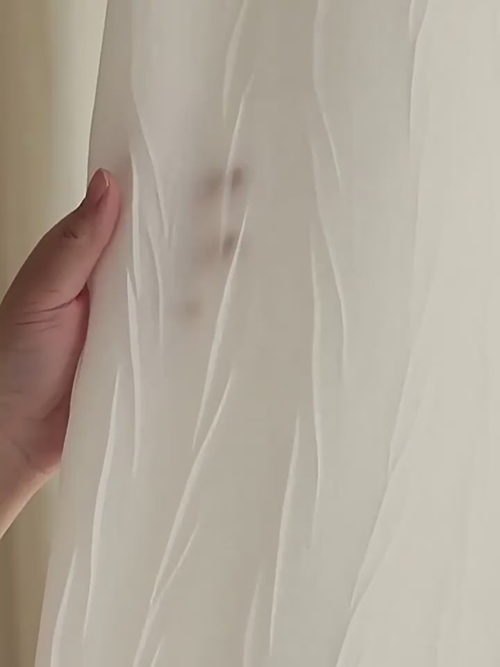 Zoom sur un voilage blanc froissé avec une main en transparence pour illustrer la légèreté et la finesse du tissu.