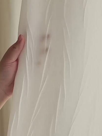 Zoom sur un voilage blanc froissé avec une main en transparence pour illustrer la légèreté et la finesse du tissu.
