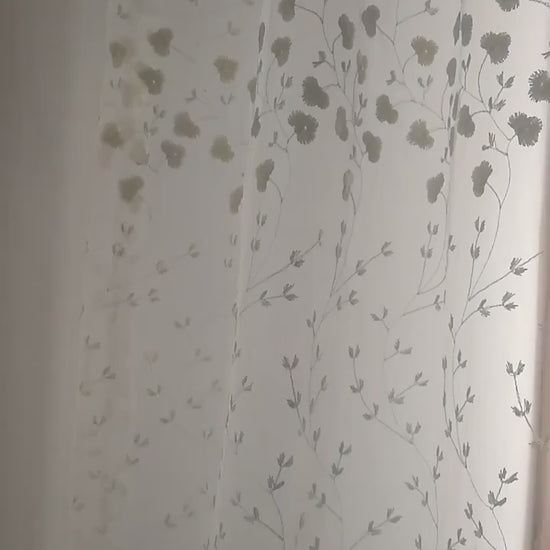 Zoom sur un voilage blanc cassé à fleurs brodées illuminé par la lumière naturelle.
