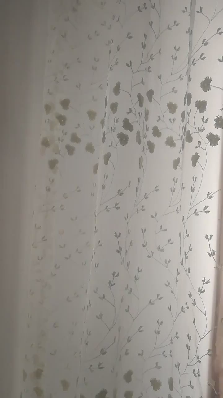 Zoom sur un voilage blanc cassé à fleurs brodées illuminé par la lumière naturelle.