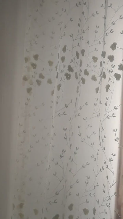 Zoom sur un voilage blanc cassé à fleurs brodées illuminé par la lumière naturelle.